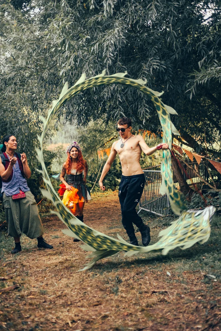 A performer rolling a serpent hoop down the woodland path